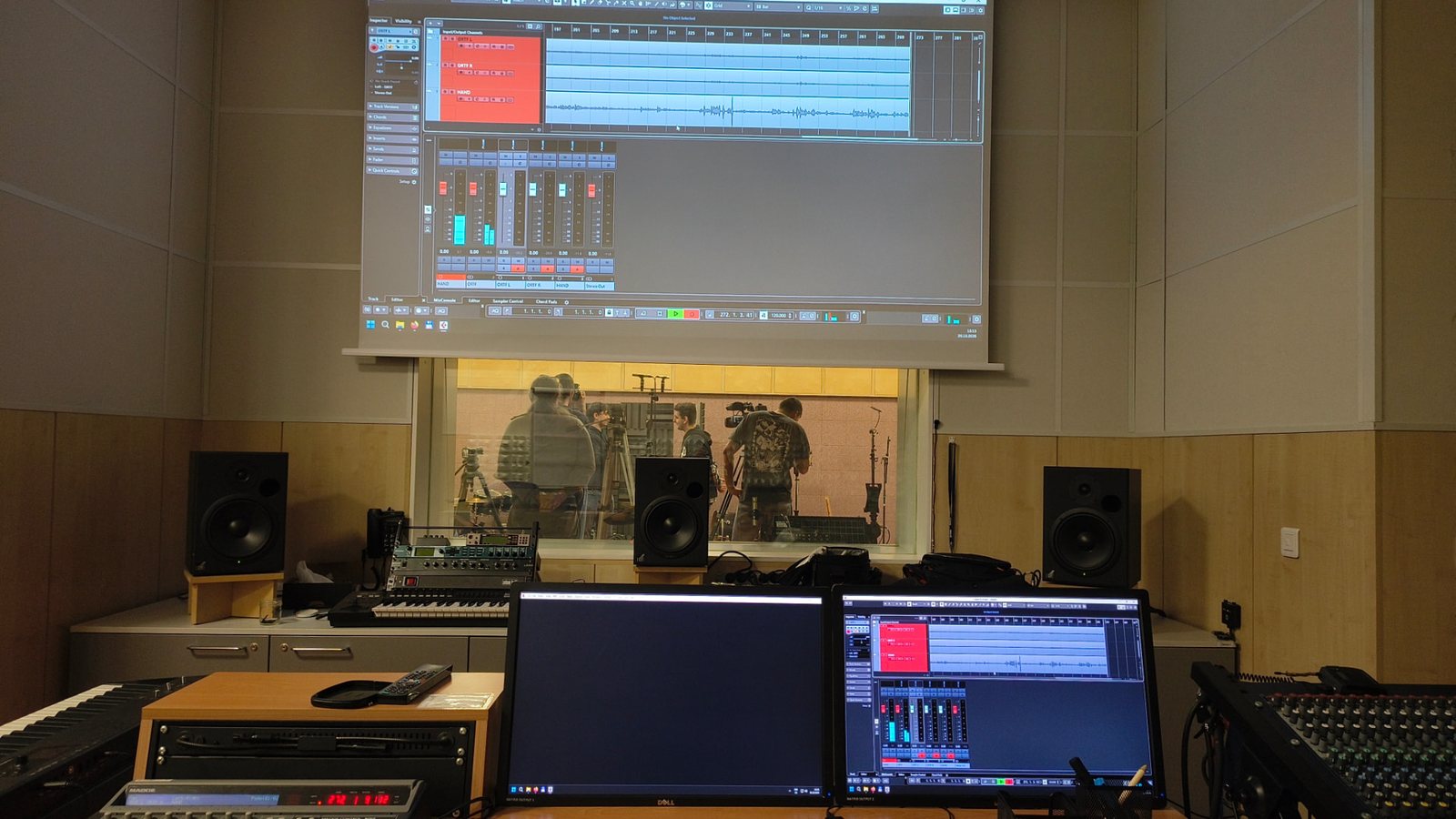 Pohled z režie studia, na promítacím plátně je otevřené DAW Cubase, skrz okno je vidět do nahrávací místnosti